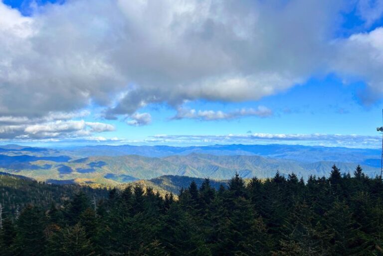 Great Smoky Mountains National Park 3 day itinerary includes this viewpoint from Kuwohi. A view from above with folige covered mountains in the distance. Specks of orange are starting to appear