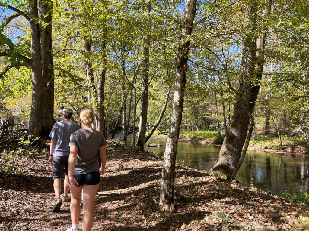 two people walking on a flat nature trail in the trees with a small river to the right on them on an easy hike in Great Smoky Mountains National Park