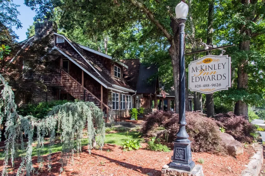 a charming wooden exterior on an inn.  It's surrounded by garden plants and trees, with a sign out from hanging off  a lamp post that says "McKinley INN Edwards".  This inn is one of the best places to stay in Great Smoky Mountains National Park on the south side
