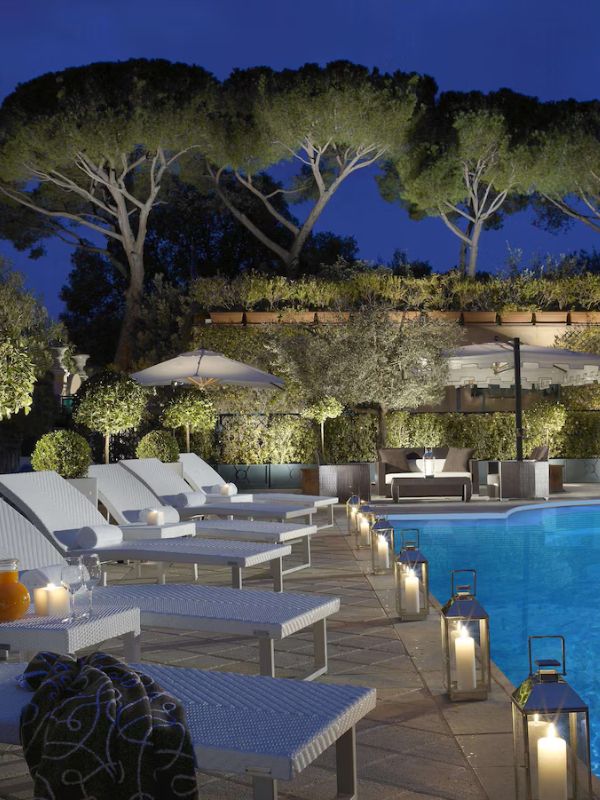 Parco dei Principi Grand Hotel in Rome Italy.  nighttime view of lounge chairs along a pool.  Large trees in the back