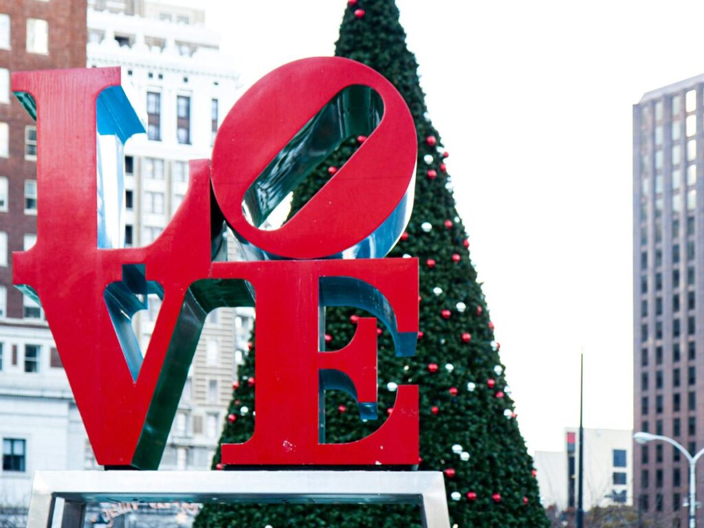 letters LO stacked on top of VE for the red love sign in Philadelphia.  A tall cone shaped, decorated christmas tree is behind the Love sign