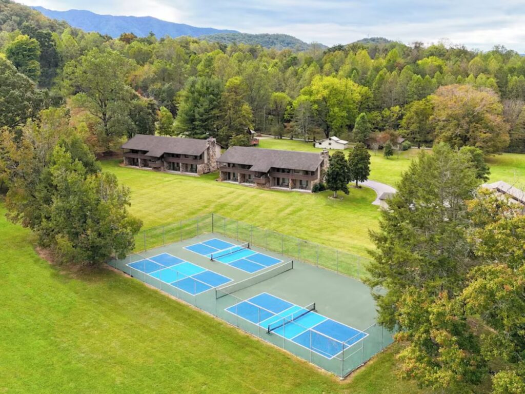 aerial view of a hotel property.  2 brown buildings sit on a vast landscape of green grass.  In front are 3 tennis courts